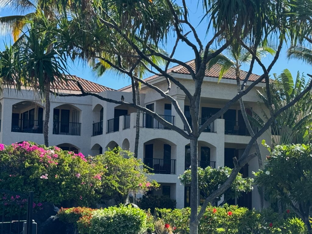 Condo complex, white with red roofs in Waikoloa with flower trees and palms fronting it.