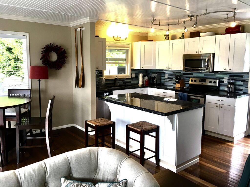 Interior of house showing a kitchen with modern accents including black granite, white cabinets, multi-colored blue backsplash, dark brown wood classic wood floors