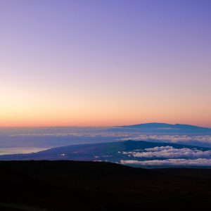 Twilight aerial view of Maui's 10,500' Haleakala Mountain off in the distance, taken from the top of Mauna Kea with an optical telescope to the left and the Pacific Ocean off in the distance below it.