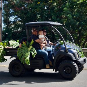Faimly in an offroad blue vehicle adorned with palm fronds in a Kamehameha day parade in Hawi, Hawaii