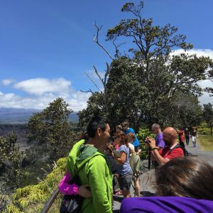 People at the Halemaumau Caldera lookout with blue skies and Mauna Loa off in the distance, Kilauea Volcano