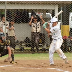 Honokaa High School Junior baseball player at bat about to hit a home run with Kohala high school team watching on
