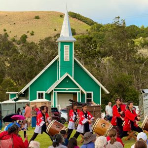 Waimea festival with japanese drum group dressed in red and white fronting a traditional, old green and white church and the surrounding green hillside of Waimea, Hawaii