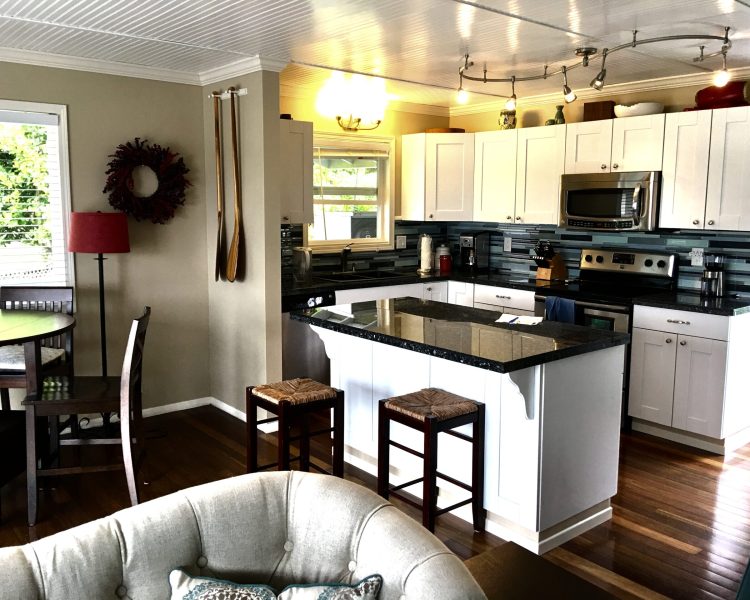 Interior of house showing a kitchen with modern accents including black granite, white cabinets, multi-colored blue backsplash, dark brown wood classic wood floors
